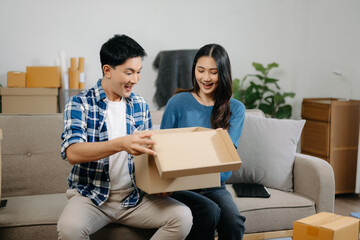 Young couple with big boxes moving into a new house, new apartment for couple, young asian man and woman helping to lift boxes on sofa .