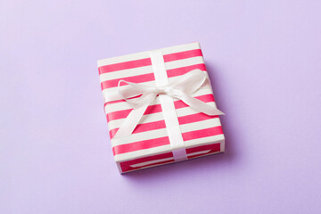 Obraz premium wrapped Christmas or other holiday handmade gift box in color paper with ribbon on colored background. Present box, decoration of gift on colored table, top view with copy space