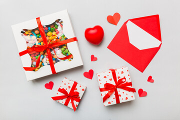 Red envelope with candy and gift box and Valentines hearts on colored background. Flat lay, top view. Romantic love letter for Holiday concept