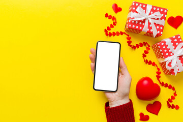 Woman hand holding mobile phone with blank screen on colored background with hearts, valentine day...