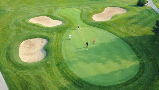 A group of four men play golf at a prestigious country club. Top view of golf course and four players on it. Leisure for business relations, active recreation of four friends at the golf club. Aerial