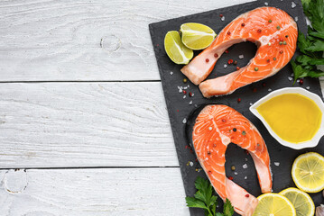 Raw salmon steaks with lemon, herbs and spices on black slate board on white wooden table. Cooking...