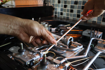 Close up of a technician's hand repairing a broken cooktop or stovetop