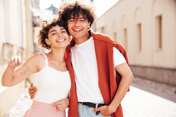 Naklejka premium Young smiling beautiful woman and her handsome boyfriend in casual summer white t-shirt and jeans clothes. Happy cheerful family. Female having fun. Couple posing in the street background. Walking