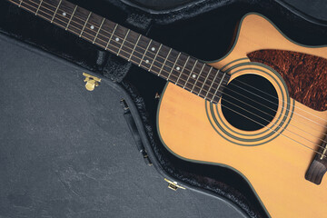 Acoustic guitar in a protective case on a dark background, top view.