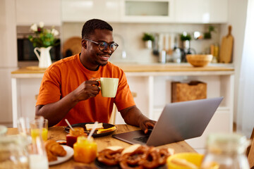 African American man using laptop while enjoying breakfast at home