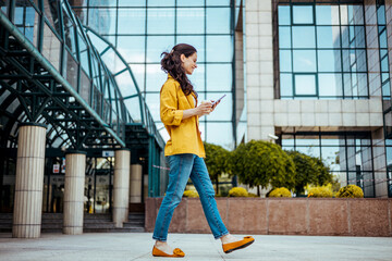 Shot of a fashionable young woman using her cellphone while walking through the city. Beautiful mid...