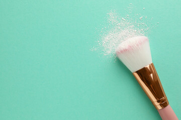 Makeup brush with rice loose face powder on turquoise background, top view. Space for text