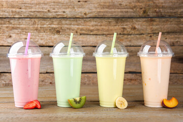 Plastic cups with different tasty smoothies and fresh fruits on wooden table