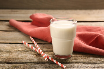 One glass of tasty milk, straws and napkin on wooden table