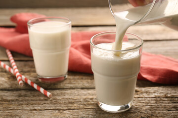Pouring tasty milk into glass on wooden table, closeup
