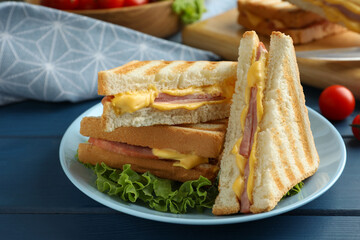 Tasty sandwiches with ham, melted cheese and lettuce on blue wooden table, closeup