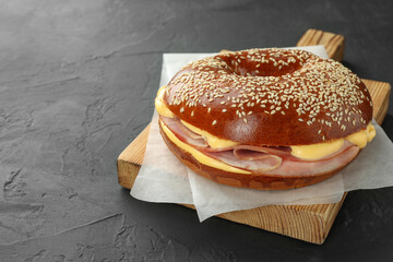 Delicious bagel with ham and cheese on grey textured table, space for text