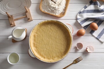 Pie tin with fresh dough and ingredients on white wooden table, flat lay. Making quiche