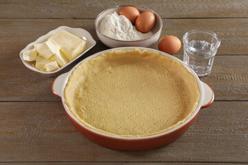 Making quiche. Baking dish with fresh dough and ingredients on wooden table
