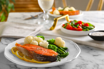 Healthy meal. Tasty grilled salmon with vegetables and lemon served on white marble table