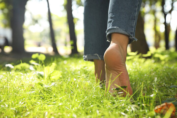 Woman walking barefoot on green grass in park, closeup. Space for text