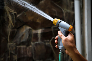 Close up of an asian man's hand watering plants around his house with a garden hose