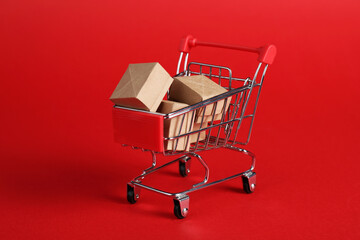 Small metal shopping cart with cardboard boxes on red background © New Africa