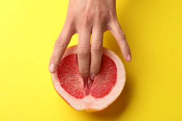 Woman touching half of grapefruit on yellow background, top view. Sex concept