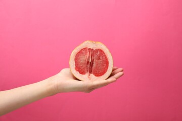 Woman holding half of grapefruit on pink background, closeup. Sex concept