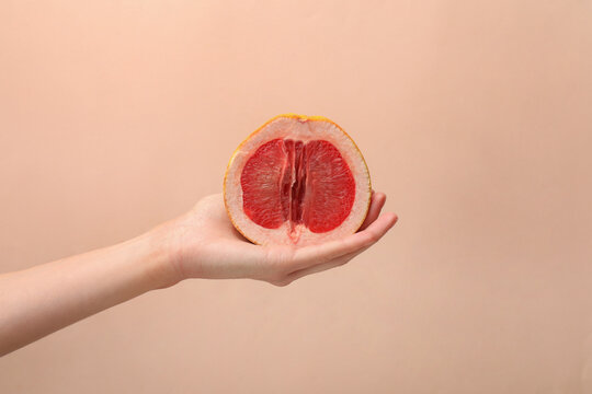 Woman holding half of grapefruit on beige background, closeup. Sex concept