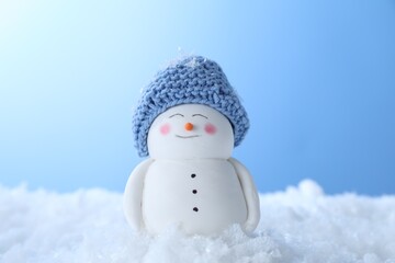 Cute decorative snowman on artificial snow against light blue background, closeup