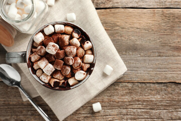 Delicious hot chocolate with marshmallows and cocoa powder in cup on wooden table, flat lay. Space for text