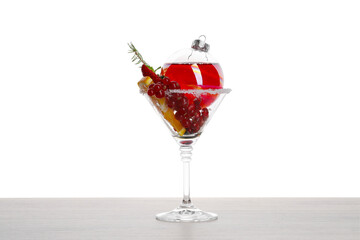Creative presentation of Christmas Sangria cocktail in bauble and glass on light wooden table against white background