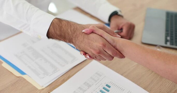 Businessman shaking woman hand over table with financial report