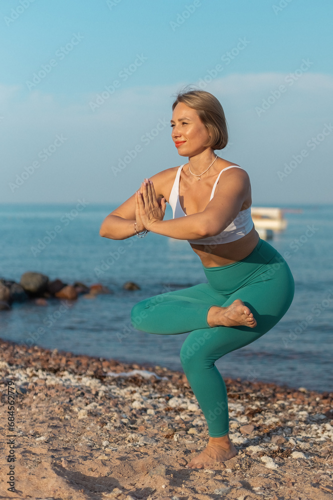 Sticker Young beautiful woman performing balance yoga position on the beach