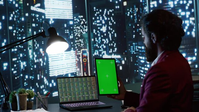 Auditor holding tablet with blank greenscreen display, trying to develop business capital from his office with panorama. Economist looking at blank chromakey copyspace screen on device.
