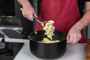Man chef, donned in a red apron, skillfully mashes boiled potatoes in a pot, creating smooth, homemade mashed potato. The scene radiates culinary mastery and the joy of crafting a comforting dish.