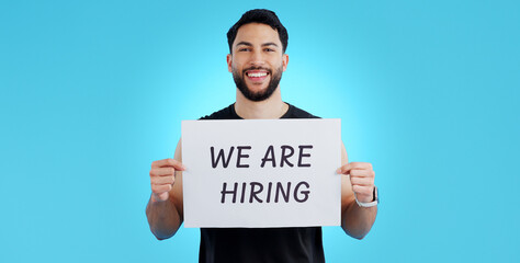 Portrait, smile and man with we are hiring, poster or announcement in studio on blue background. Recruitment, banner and face of male model with news, announcement or business, opportunity or offer