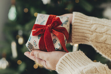 Merry Christmas! Woman in cozy sweater holding stylish christmas gift in festive wrapping paper...