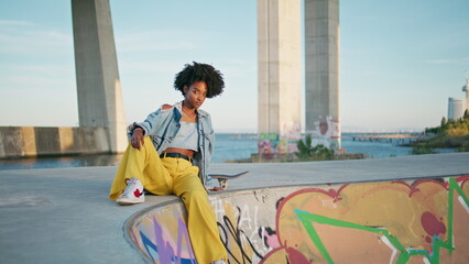 Cool african model posing at urban backdrop close up. Hipster sitting skate park