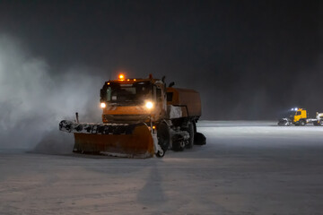 Snowplow trucks cleans night airport apron in a blizzard