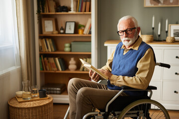 Elderly man with in wheelchair reading a book at home at home