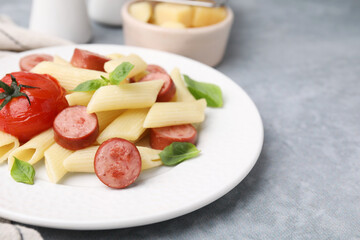 Tasty pasta with smoked sausage, tomato and basil on light grey table, closeup. Space for text