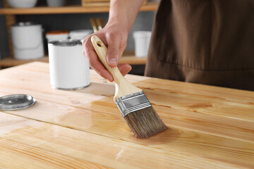 Man varnishing wooden surface with brush indoors, closeup