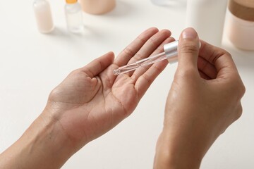 Woman applying cosmetic serum onto her hand at white table, closeup