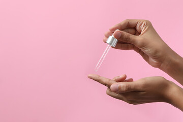 Woman applying cosmetic serum onto her finger on pink background, closeup. Space for text - obrazy, fototapety, plakaty