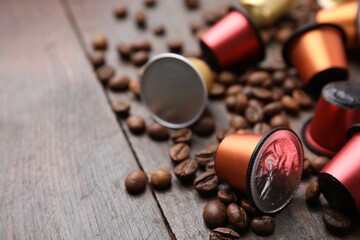 Many coffee capsules and beans on wooden table, closeup. Space for text