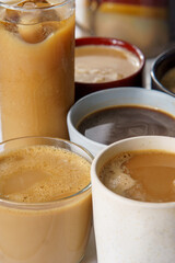 45 degree viev of several coffees. Some of them have milk, some are black, hot, iced, on a white tableccloth