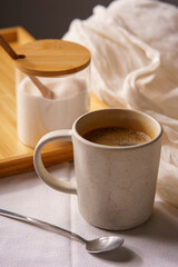 Cup of black coffe served on a white mug. There is a saucer with white sugar on a wooden tray, and everything lays on a white tablecloth. 45 degree viewo