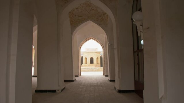 Ancient wooden doors with oriental ornaments open into a hall with columns of the Mir-i-Arab Madrasa complex.