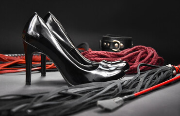 Black shiny high heels, whip and rope stock photo images. Set of erotic toys for BDSM on a dark...