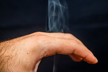 Smoke envelops a man's hand close-up on a black background	
