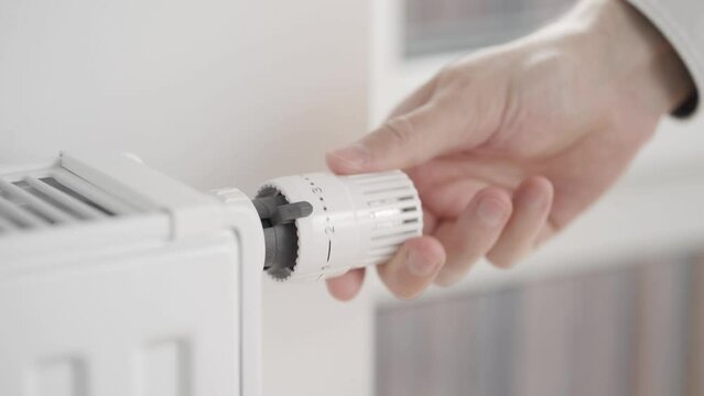The man closes the window and turns on the heating in the house by turning the radiator thermostat valve to the maximum heating value. The start of the heating season.