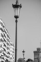 Fototapeta na wymiar View of a lantern, residential buildings and the famous White Tower, also known as Lefkos Pyrgos in Thessaloniki Greece in black and white